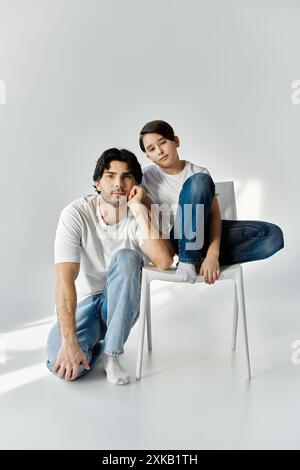 Vater und Sohn verbringen gute Zeit miteinander, sitzen auf einem weißen Stuhl in einem hellen Studio. Stockfoto