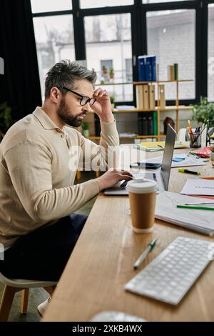 Ein gutaussehender Geschäftsmann mit Bart arbeitet an einem Laptop an seinem modernen Schreibtisch. Stockfoto