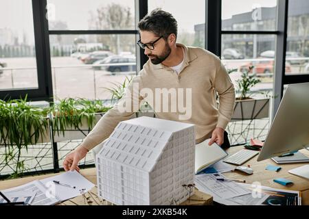 Ein gutaussehender bärtiger Geschäftsmann in Brille arbeitet in einem modernen Büro und untersucht ein Baumodell auf seinem Schreibtisch. Stockfoto