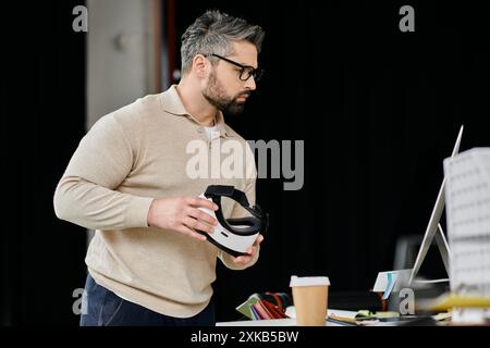 Ein gutaussehender Geschäftsmann mit Bart hält ein weißes Virtual-Reality-Headset in einer modernen Büroumgebung. Stockfoto