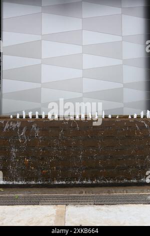 Brunnen außerhalb des Gebäudes und eine graue Wand im Hintergrund, Wasser fällt aus dem Brunnen durch die Felsschichten. Stockfoto