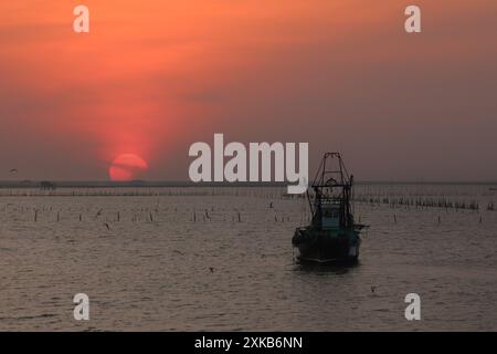 Ein einheimisches Fischerboot liegt am Meer und dem Sonnenuntergang in der Gegend der Muschelfarm ​​a in der Provinz Chonburi in Thailand. Stockfoto