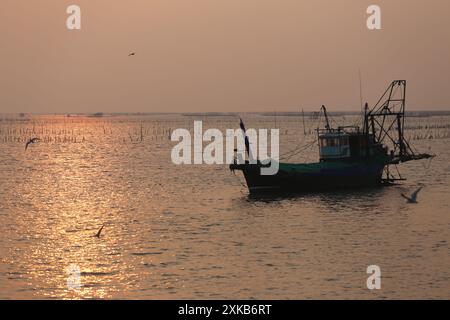 Ein einheimisches Fischerboot liegt am Meer und dem Sonnenuntergang in der Gegend der Muschelfarm ​​a in der Provinz Chonburi in Thailand. Stockfoto