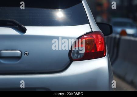 Rote Lichter auf der Rückseite einer bronzefarbenen Limousine, während der Motor ausgeschaltet war, und Lichter reflektierten auf der Heckscheibe des Autos. Stockfoto