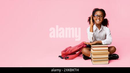 African Schoolgirl Heben Hand Sitzen Bei Bücher Über Gelben Hintergrund Stockfoto