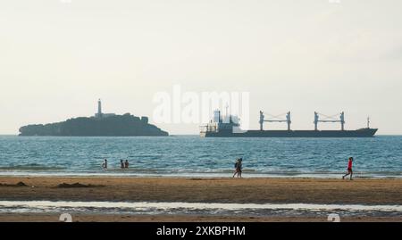 Das Massengutschiff Alma verlässt den Hafen von Santander mit dem Leuchtturm der Insel Mouro vom Strand Somo Ribamontán al Mar Cantabria aus gesehen Stockfoto