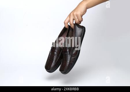 : Leder-Loafers tragen Schuhe, die auf hellem Hintergrund in der Hand gehalten werden Stockfoto