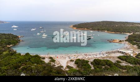 Blick auf die Bucht von Portese auf Caprera, auf Sardinien, mit Freizeitbooten, die im türkisfarbenen Wasser liegen und viele Menschen, die sich sonnen und genießen Stockfoto