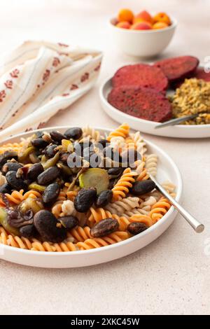 Glutenfreie Nudeln mit gebackenen Bohnen und Zucchini, gepaart mit Rübenpfannkuchen mit Sonnenblumenkorn-Hummus. Diese gesunde vegetarische Mahlzeit ist sowohl köstlich als auch nährend Stockfoto