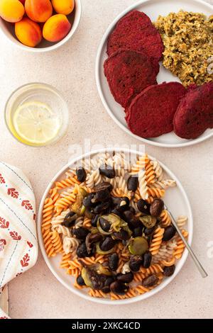 Glutenfreie Nudeln mit gebackenen Bohnen und Zucchini, gepaart mit Rübenpfannkuchen mit Sonnenblumenkorn-Hummus. Diese gesunde vegetarische Mahlzeit ist sowohl köstlich als auch nährend Stockfoto