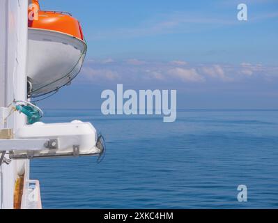 Rettungsboot auf dem Deck einer Fähre. Leben retten mit dem Wasserkonzept. Seitenansicht vor dem Hintergrund des Himmels und ruhiges Meer bei sonnigem Wetter Stockfoto