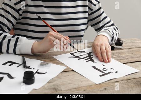 Kalligraphie. Frau mit Pinsel und Tintenfass, die chinesische Hieroglyphen auf Papier auf Holztisch schreibt, Großaufnahme Stockfoto