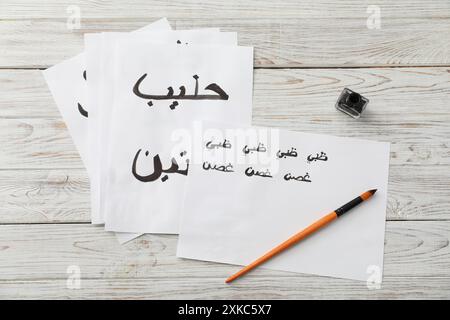 Kalligraphie. Papiere mit den Worten Milch und Antilope in arabischer Sprache, Tintenfass und Pinsel auf weißem Holztisch, flach gelegt Stockfoto