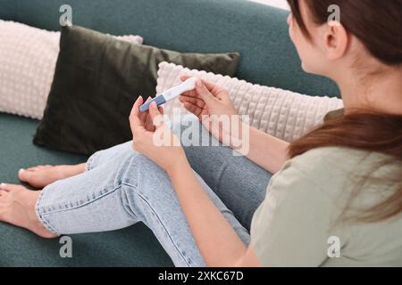 Junge Frau mit Schwangerschaftstest auf Sofa zu Hause, Nahaufnahme Stockfoto