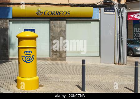 Viladecasn, SPANIEN - 22. JULI 2024: Gelbe Correos-Mailbox auf einer spanischen Stadtstraße. Im Hintergrund sehen Sie das Postamt und sein Schild. Stockfoto