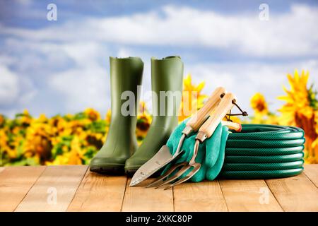 Gartenschlauch und grüne Gummistiefel und Gartenwerkzeuge auf Holztisch mit Gartenhintergrund. Stockfoto