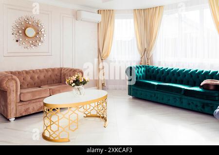 Ein wunderschön eingerichtetes Wohnzimmer mit einem weichen rosafarbenen Sofa, einem eleganten grünen Sofa und einem Blumenarrangement auf einem stilvollen goldenen und weißen Tisch. Mi Stockfoto