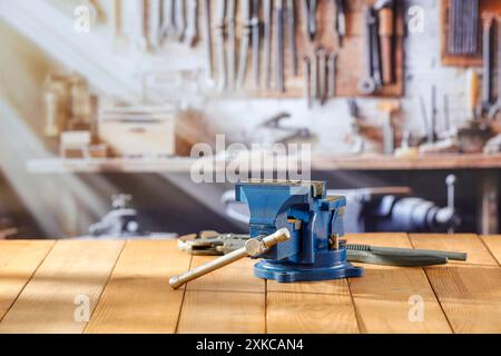 Schlosserschrauber auf Holzarbeitstisch in der Handwerkstatt. Unscharfe Wand mit Werkzeugen im Hintergrund. Stockfoto