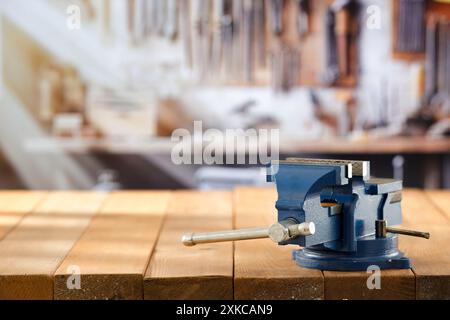 Schlosserschrauber auf Holzarbeitstisch in der Handwerkstatt. Unscharfe Wand mit Werkzeugen im Hintergrund. Stockfoto