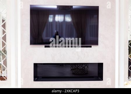Ein modernes Wohnzimmer mit einem wandmontierten Fernseher und einem elektrischen Kamin darunter. Stockfoto