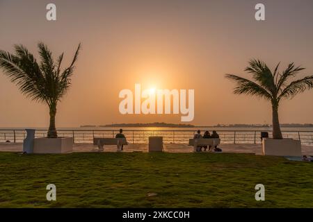 Arabische Menschen beobachten den wunderschönen Sonnenuntergang auf der Parkbank in Al Hamra Corniche in der Uferpromenade von Jeddah, Saudi-Arabien. Stockfoto