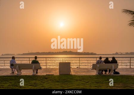 Arabische Menschen beobachten den wunderschönen Sonnenuntergang auf der Parkbank in Al Hamra Corniche in der Uferpromenade von Jeddah, Saudi-Arabien. Stockfoto