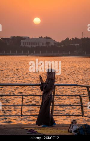 Die Paranja bedeckte muslimische Frau an der Jeddah Corniche (Uferpromenade) in Saudi-Arabien und beobachtete den wunderschönen Sonnenuntergang im Nahen Osten. Stockfoto