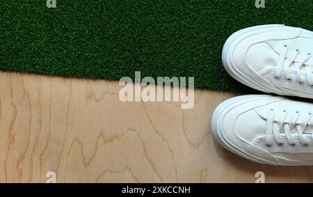 Weiße Turnschuhe auf einem Hintergrund aus Gras- und Holzstruktur, Draufsicht. Bequeme weiße Schuhe, Stoffschuhe. Ein Paar stylische weiße Sneakers aus der Nähe. Stockfoto