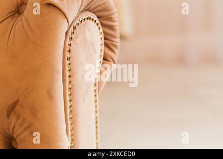 Nahaufnahme einer beigefarbenen Sofa-Armlehne mit goldener Nagelkopfverkleidung, die luxuriöse Möbeldetails in einem gemütlichen Zimmer hervorhebt. Stockfoto