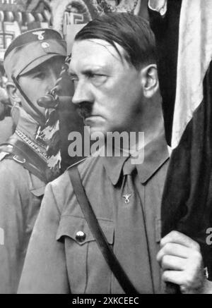 Eine Fotografie von Adolf Hitler im Jahr 1935, aufgenommen während einer feierlichen Veranstaltung, bei der er neue Standards für das NS-Militär präsentierte. Hitler betonte die Loyalität zu diesen Symbolen, die die Einheit und Stärke der Nation repräsentierten. Zu dieser Zeit hatte Hitler seine Kontrolle über Deutschland gefestigt, die nationalistische Ideologie gefördert und das Land auf eine aggressive Expansion vorbereitet. Stockfoto