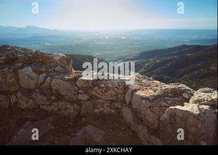 Das Bild zeigt eine alte Steinmauer mit einem atemberaubenden Blick auf eine ruhige Bergkette unter klarem Himmel. Dieser malerische Ort zeigt die Schönheit von n Stockfoto