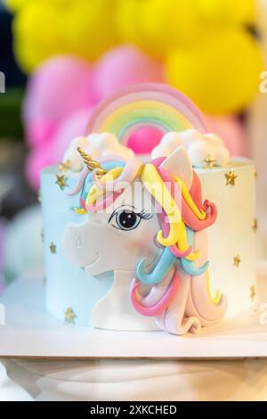 Einhorn-Geburtstagskuchen mit Regenbogenfarben: Rosa und gelbe Ballons im unscharfen Hintergrund. Stockfoto