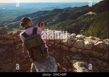 Ein Backpacker und Fotograf fängt die malerische Berglandschaft von einem felsigen Aussichtspunkt ein. Das Bild weckt Gefühle von Abenteuer, Entdeckungen und na Stockfoto