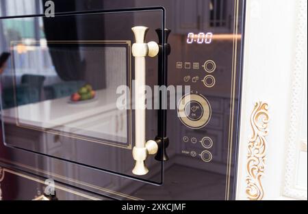 Nahaufnahme einer eingebauten Mikrowelle mit eleganten goldenen Griffen und komplizierten Designelementen. Stockfoto