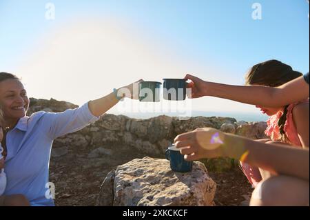 Eine Gruppe von Freunden, die einen schönen Tag mit Kaffee im Freien genießen und mit Tassen auf einem felsigen Hügel unter der Sonne anstoßen. Stockfoto