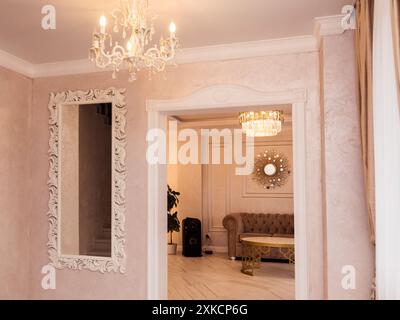 Eleganter Flur mit Kronleuchter und verziertem Spiegel und Blick in ein stilvolles Wohnzimmer. Minsk, Weißrussland - 14. August 2023 Stockfoto