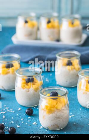 Reispudding mit Mango in Dessertgläsern auf blauem Hintergrund, Sommerdessert, vertikal Stockfoto