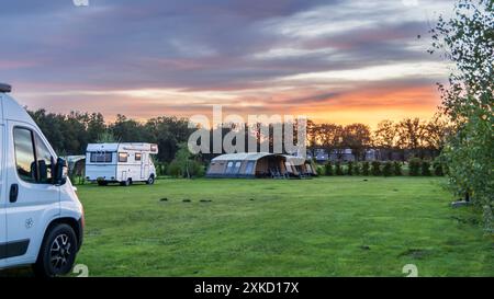Panoramalandschaft mit wunderschönem Sonnenuntergang auf einem Bauerncamping mit Familienzelten und einem alten Wohnmobil in Drenthe, Niederlande Stockfoto