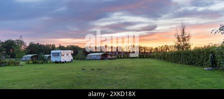 Panoramalandschaft mit wunderschönem Sonnenuntergang auf einem Bauerncamping mit Familienzelten und einem alten Wohnmobil in Drenthe, Niederlande Stockfoto