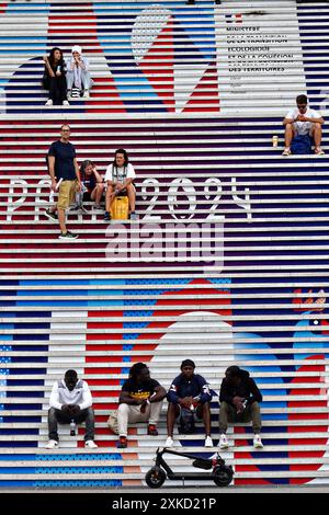 Paris, Frankreich. Juli 2024. Die Menschen sitzen auf den Stufen des La Defence Arch, der am 22. Juli 2024 in Paris mit den Olympischen Zeichen von Paris 2024 geschmückt ist. Die Eröffnungszeremonie findet am 26. Juli statt, 100 Jahre nach dem letzten Austragungsort der Spiele in Paris. Foto: Richard Ellis/UPI Credit: UPI/Alamy Live News Stockfoto