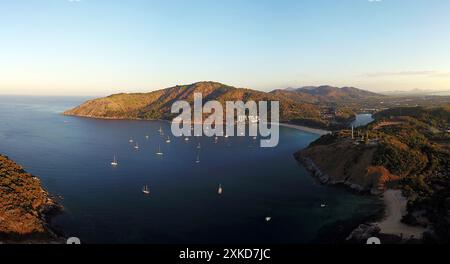 Ein malerischer Blick aus der Luft auf eine Bucht mit vor Anker liegenden Yachten, umgeben von üppigen Hügeln und klarem Himmel bei Sonnenuntergang Stockfoto