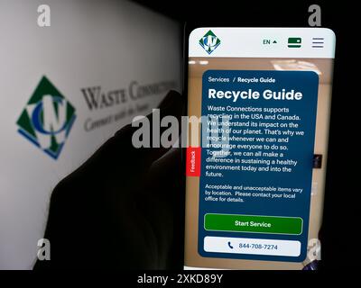 Person, die ein Mobiltelefon hält, mit der Webseite des US-Recyclingunternehmens Waste Connections Inc. Vor dem Firmenlogo. Konzentrieren Sie sich auf die Mitte des Telefondisplays. Stockfoto