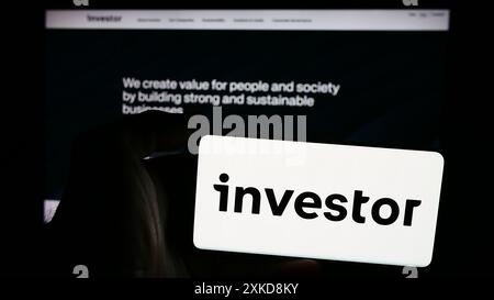 Person mit Smartphone und Logo der schwedischen Investmentgesellschaft Investor ab vor der Website. Schwerpunkt auf dem Display des Telefons. Stockfoto
