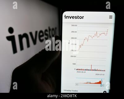 Person, die ein Smartphone hält und die Webseite der schwedischen Investmentgesellschaft Investor ab vor dem Geschäftslogo zeigt. Konzentrieren Sie sich auf die Mitte des Telefondisplays. Stockfoto