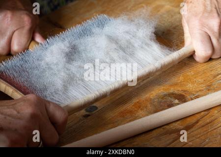 Die gekarstete Rohwolle wird mit einem runden Stock aus der Handkardiermaschine entfernt. Stockfoto