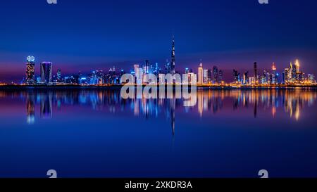 Ein atemberaubender Blick bei Nacht auf Dubais Skyline, mit hohen Gebäuden, die vor einem dunkelblauen Himmel beleuchtet werden und deren Reflexionen sich im ruhigen Wasser spiegeln Stockfoto