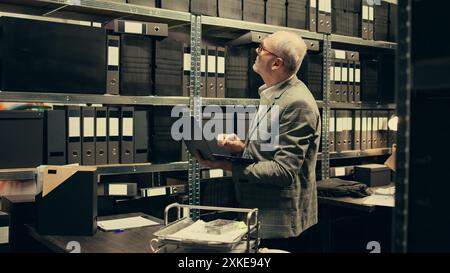 Privatdetektiv liest Rechtsdokumente und Bundesnotizen im Archivraum, arbeitet an Strafverfahren. Der Polizeibeamte eröffnet Ermittlungen, um einen Verdächtigen zu finden, Bürokratie. Kamera A.. Stockfoto