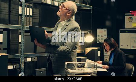 Privatdetektiv sucht nach Akten basierend auf Fallnamen im Archiv, sucht nach Rechtsdokumenten und Verschlusssachen auf dem Laptop. Agent arbeitet an Kriminologie im Vorfallsraum. Kamera A.. Stockfoto