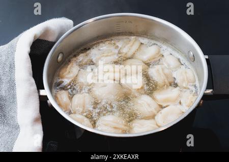 Teigtaschen Pelmeni mit Hackfleisch Füllung kochen in heißer Brühe in Stahltopf auf Herd in der Küche, Kochfortschritt, sprudelndes Wasser Stockfoto