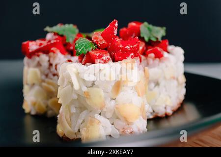 Nahaufnahme von Sushi-Brötchen, garniert mit Erdbeerwürfeln und garniert mit grünen Blättern auf einem dunklen Teller und Hintergrund, Koch-Restaurant-Gericht Stockfoto